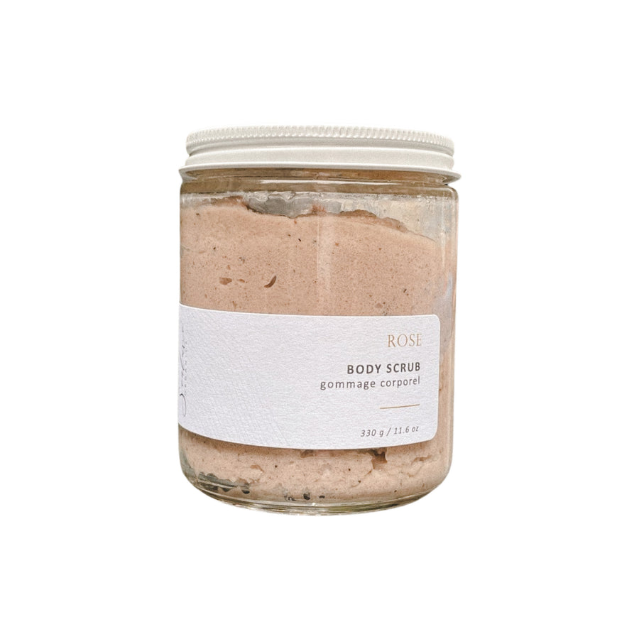 A clear glass jar with a white label and a black cap containing a pale pink and black scrub with the words "Ritual Rose" written on the label. The background is plain white.