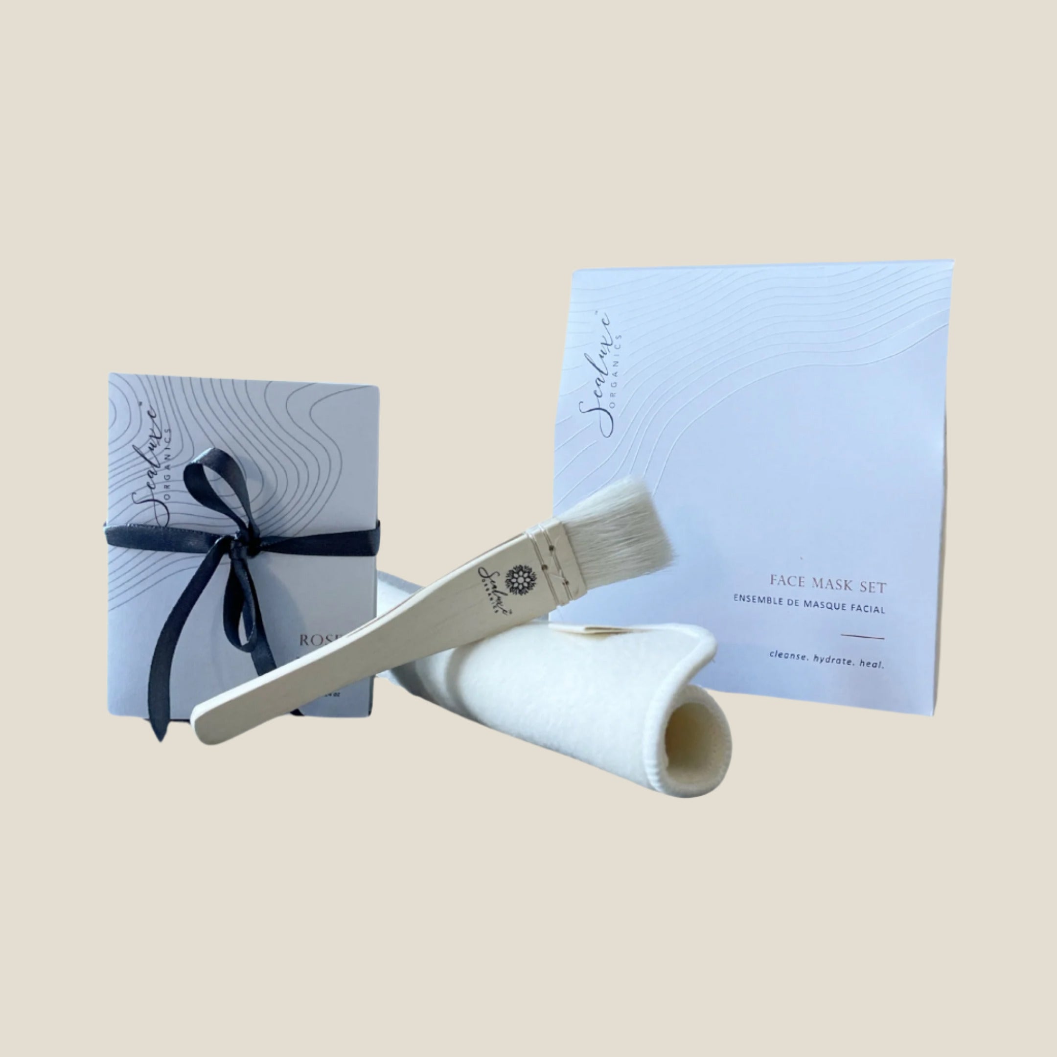 A Face Mask Gift Set including four single use face masks in sachets, tied with a black ribbon, and a face mask brush, displayed on a white background.