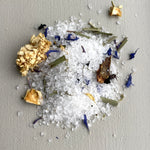 White bath salts with gold and purple flowers on a gray background
