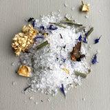 White bath salts with gold and purple flowers on a gray background