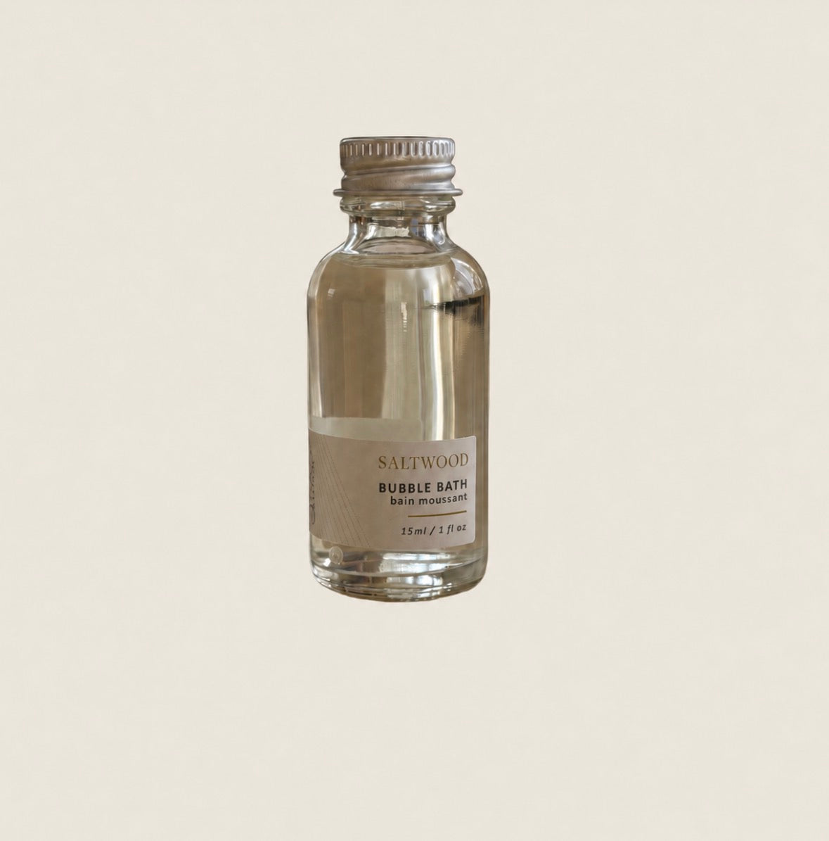 A small clear glass bottle of SALTWOOD Bubble Bath with a silver metal cap and a beige label, centered on a solid light beige background.