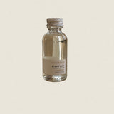 A small clear glass bottle of SALTWOOD Bubble Bath with a silver metal cap and a beige label, centered on a solid light beige background.