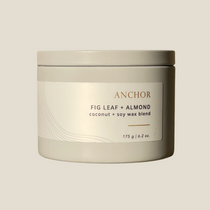 A metal tin container with a lid, labeled 'Anchor Fig Leaf + Almond', indicating a coconut soy wax blend candle.