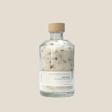 A clear glass jar with a wooden lid, labeled as 'Lavender Vanilla Bath Salt', containing white bath salts with visible small botanical particles.