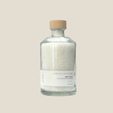 A clear glass jar with a wooden lid containing bath salts. The label on the jar reads 'Lemon Lavender Bath Salts'