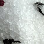 Close-up of a crystal formation with a black tool on a white background