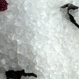 Close-up of a crystal formation with a black tool on a white background
