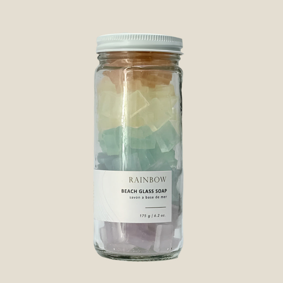 Glass jar with rainbow-colored beach glass soap on a beige background
