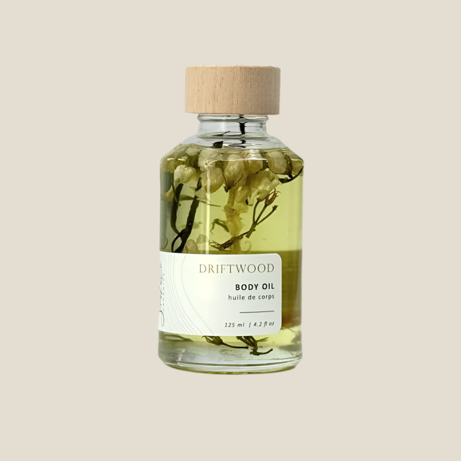 Bottle of Driftwood body oil with a wooden cap on a light gray background