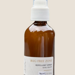 Brown spray bottle labeled 'Bug-Free Zone' on a light surface with a blurred green background