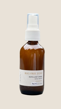 Brown spray bottle labeled 'Bug-Free Zone' on a light surface with a blurred green background