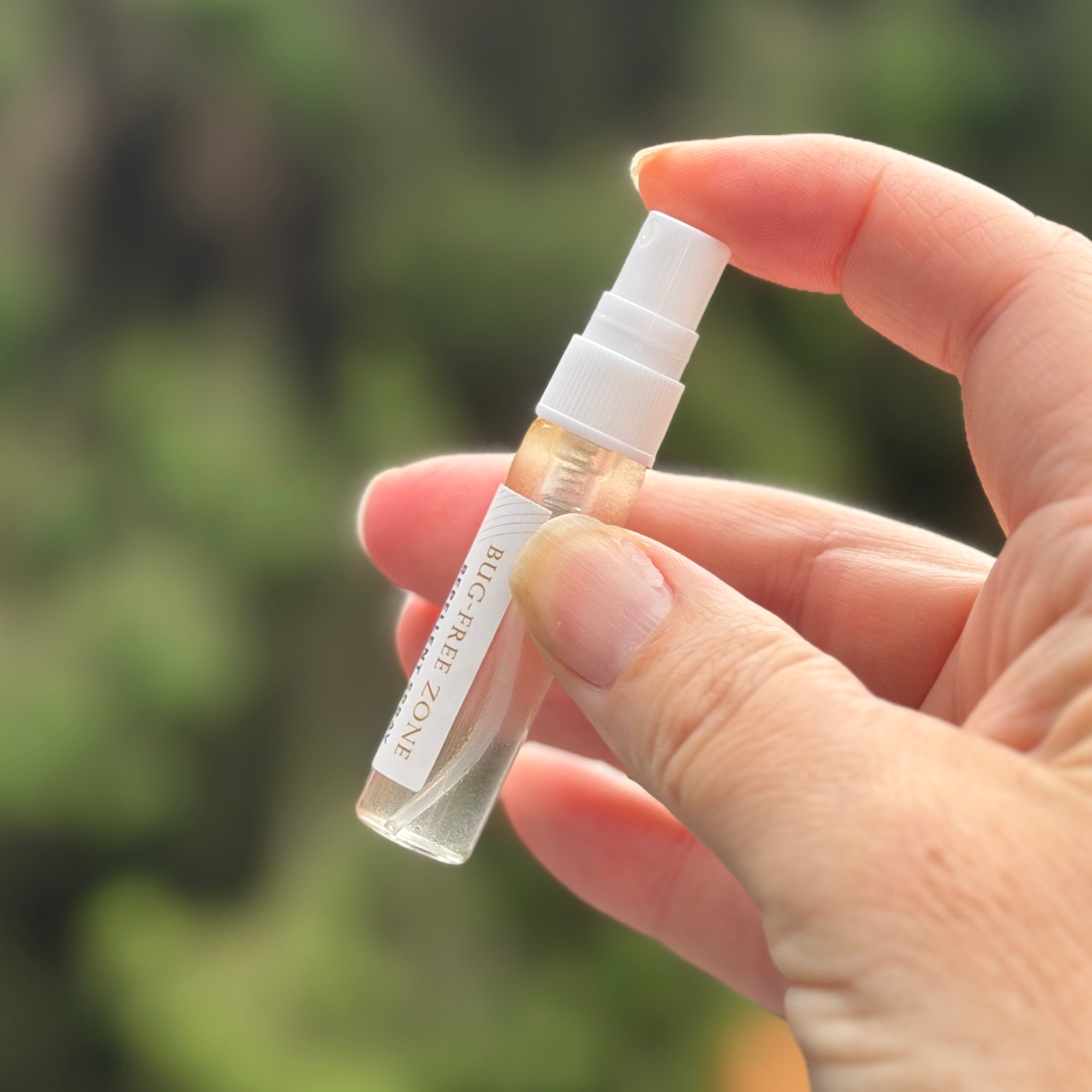 Hand holding a small spray bottle with a blurred green background