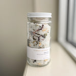 A glass jar with a metal lid labeled 'FOREST BATHING BATH TEA' containing white bath salts and natural botanicals.