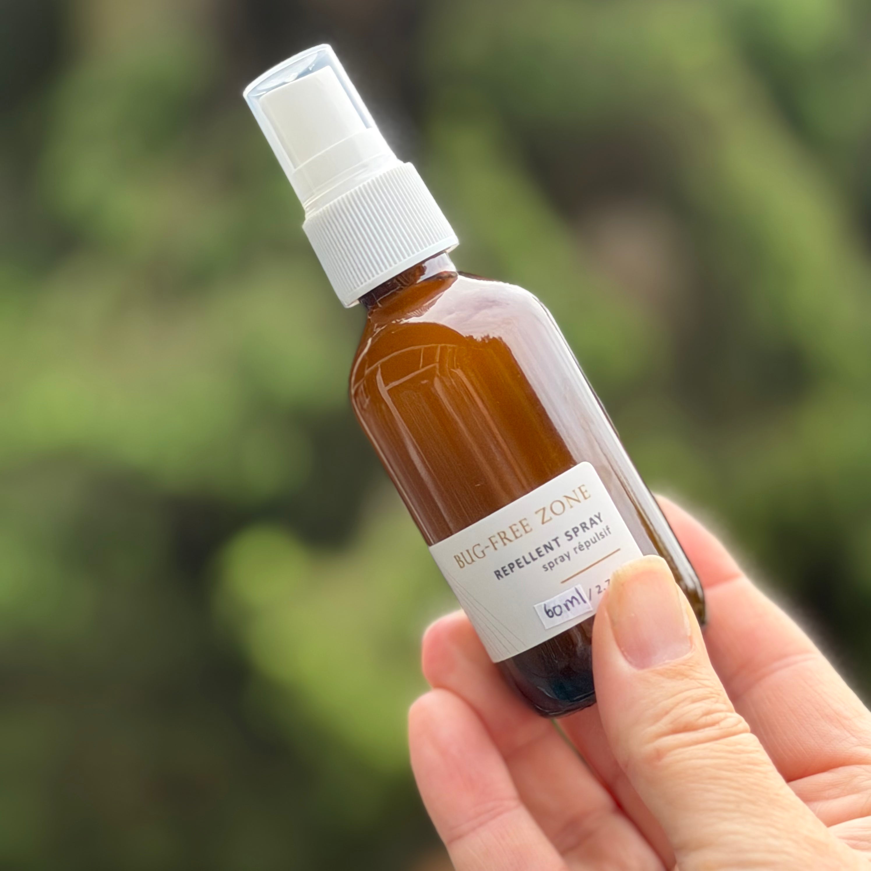 Hand holding a small brown bottle with a white spray nozzle against a blurred green background