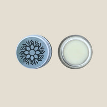 The image shows a glass jar with a metal lid, containing a natural lip balm. The lip balm is white and there is a snowflake design on the lid.