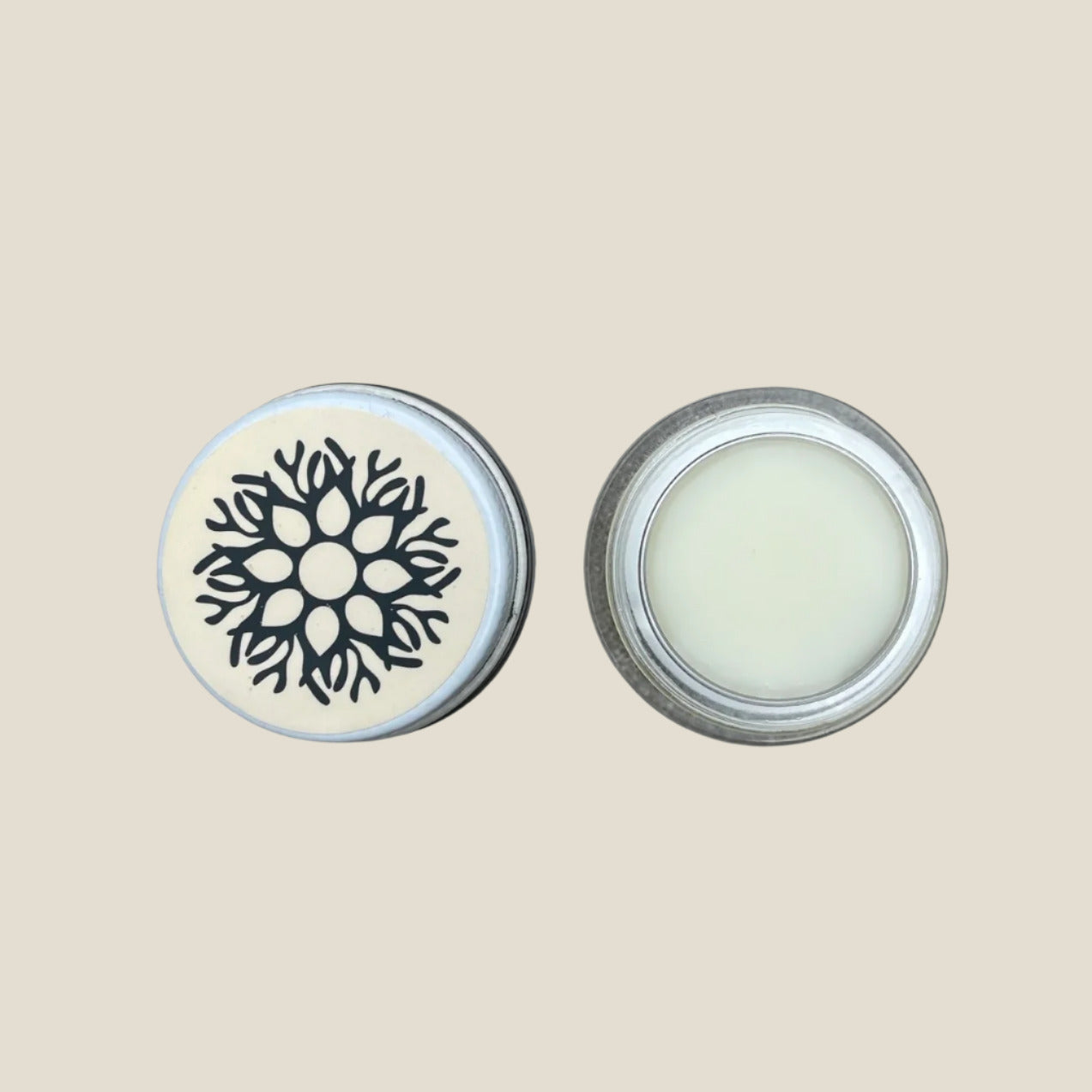 A small open jar of lip balm with a white product inside, next to its lid which has a floral design. The jar is placed on a white background.