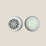 A small open jar of lip balm with a white product inside, next to its lid which has a floral design. The jar is placed on a white background.