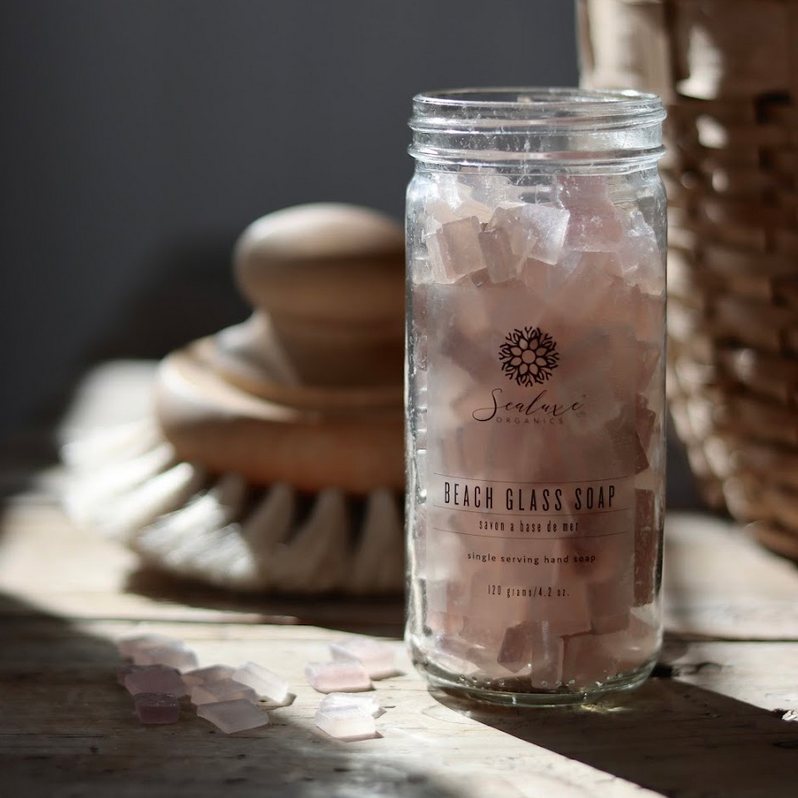 Sealuxe's rose beach glass soap in a clear jar sitting in the sun with shadows