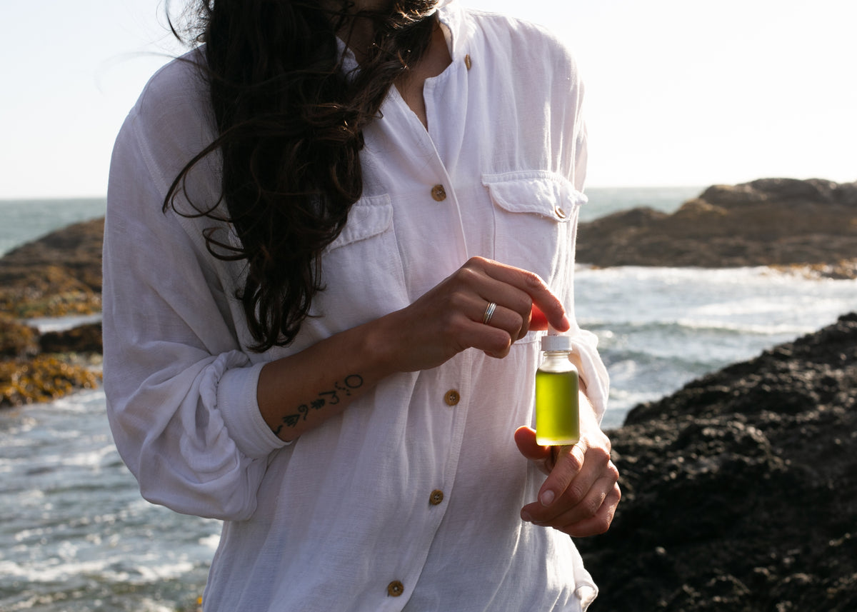 Woman on a BC ocean coastline holding Sealuxe body oil — wild-harvested seaweed-infused body oil