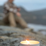 Sealuxe candle burning on a rock with a blurred person in the background