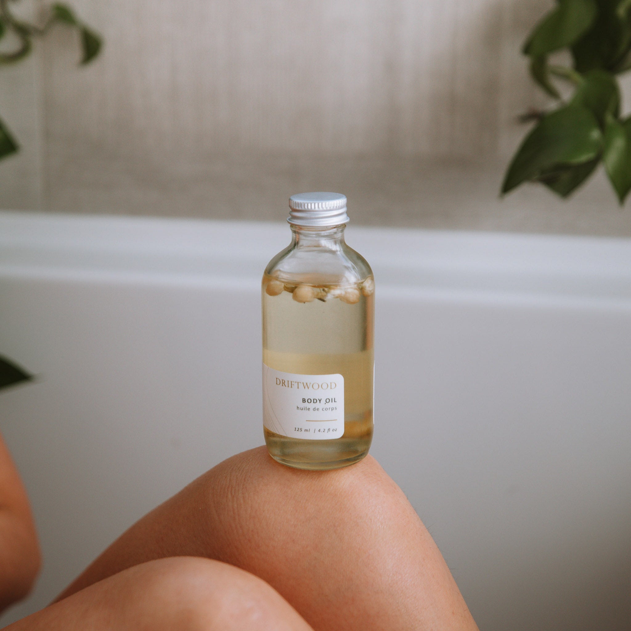 Sealuxe Driftwood Body Oil bottle resting on a bath tray beside a drawn bath