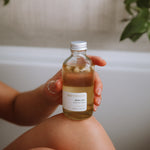 Sealuxe Driftwood Body Oil bottle placed in a serene bath setting with warm tones