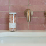 Sealuxe Rose Beach Glass Soap jar with pink sea glass soap pieces on a pink tiled bath ledge beside a gold faucet