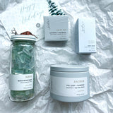 Flat lay of Sealuxe 'Sand and Snow' winter beach gift set, featuring Aqua Beach Glass soap, Ocean Flora soap bar, Westcoast White candle, and Salty Sea bath bomb, artistically arranged to evoke a coastal winter escape.