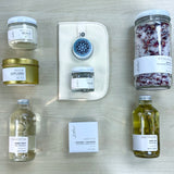 Flat lay view of Sealuxe Spa at Home gift box products including bubbles, body oil, bath tea, bath bomb, Driftwood butter, seaweed face mask, cloth, Gold Anchor candle, and lip balm, artistically displayed for a full spa experience.
