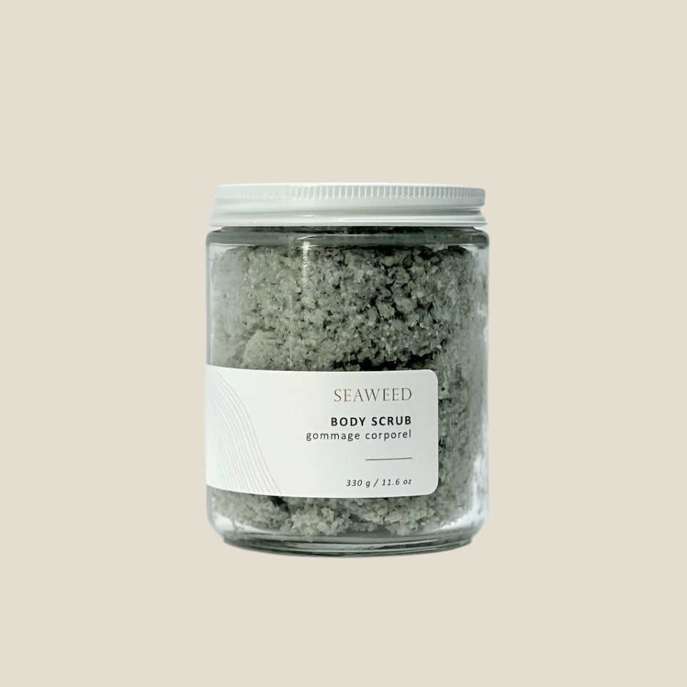 A clear glass jar with a white lid containing green-colored seaweed salt scrub. The label on the jar reads 'SEAWeed BODY SCRUB'.