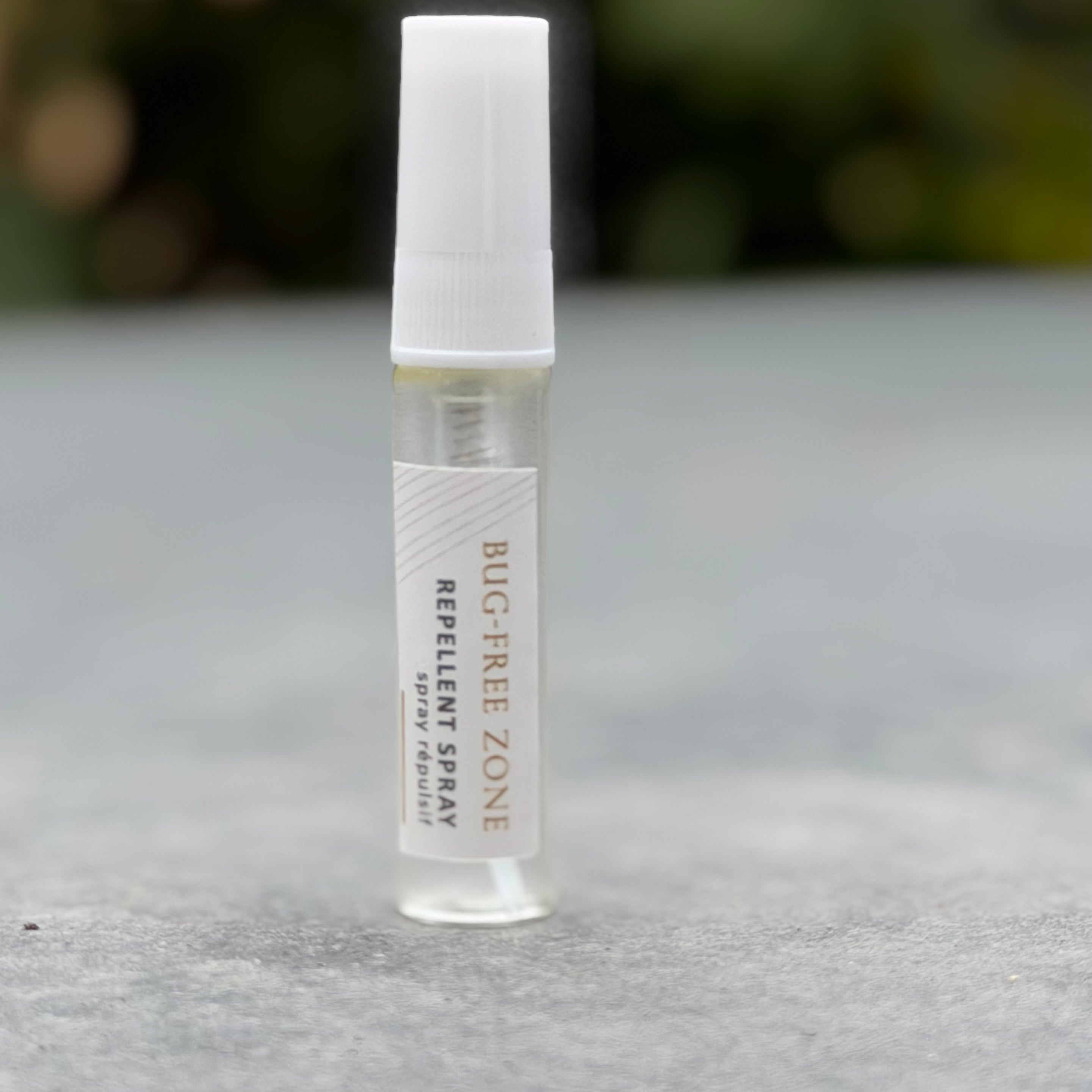 Bug-Free Zone repellent spray bottle on a gray surface with a blurred natural background