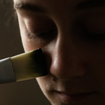 Spreading Sealuxe's charcoal face mask with a brush on cheek.