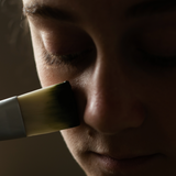 Spreading Sealuxe's charcoal face mask with a brush on cheek.